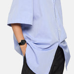 Eine Person in hellblauem Button-up-Hemd und Nadelstreifenhose trägt die Liebeskind Berlin Armbanduhr - Round Vinyl Vision mit verspiegeltem Ziffernblatt, die Hand stilvoll in die Tasche gesteckt.