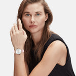 Frau mit hellbraunem Haar, die ein ärmelloses schwarzes Oberteil und eine rosafarbene LIEBESKIND BERLIN Armbanduhr - Keep Loving im skandinavischen Design von Liebeskind Berlin trägt, schaut in die Kamera.