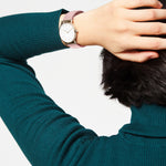 Eine Person im grünen Pullover mit der Hand auf dem Kopf trägt die LIEBESKIND BERLIN Armbanduhr - The Modern Must-Have von Liebeskind Berlin mit einem rosa Armband am Handgelenk.