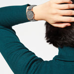 Eine Person in einem blaugrünen Pullover zeigt die LIEBESKIND BERLIN Armbanduhr - The Modern Must-Have von Liebeskind Berlin und hält ihre Hand hinter den Kopf.