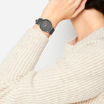 Die Person trägt einen cremefarbenen Strickpullover und eine Liebeskind Berlin Armbanduhr - The Leather One, wobei sie die Hand an ihr Ohr hält.