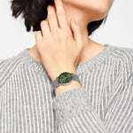 Eine Person trägt einen grau gestreiften Pullover und eine Liebeskind Berlin Armbanduhr - Color Up mit grünem Gesicht und poliertem silbernen Netzband in minimalistischem skandinavischem Design.