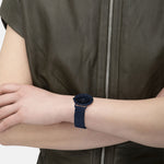 Person trägt eine ärmellose Jacke mit Reißverschluss und eine LIEBESKIND BERLIN Armbanduhr - Glitter-Special von Liebeskind Berlin mit Edelstahl-Meshband und minimalistischem Design am linken Handgelenk.