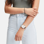 Frau in hellen Jeans und grünem Oberteil, die eine Liebeskind Berlin Classic x Trends Armbanduhr und ein Armband trägt, verschränkt lässig die Arme.