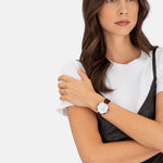 Eine Frau in weißem T-Shirt und schwarzem Kleid trägt die Liebeskind Berlin Armbanduhr - The Classy Acetat, verschränkt die Arme und schaut zur Seite.