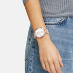 Eine Person, die eine rosafarbene Liebeskind Berlin LIEBESKIND BERLIN Armbanduhr - The Multi-Function wristwatch und eine blaue Jeans trägt und eine Hand an ihrer Seite ruhen lässt.