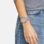 Eine Person in Jeans und einem gerippten Oberteil trägt die LIEBESKIND BERLIN Armbanduhr - The Multi-Function von Liebeskind Berlin, mit einem runden Gesicht und grauem Band.