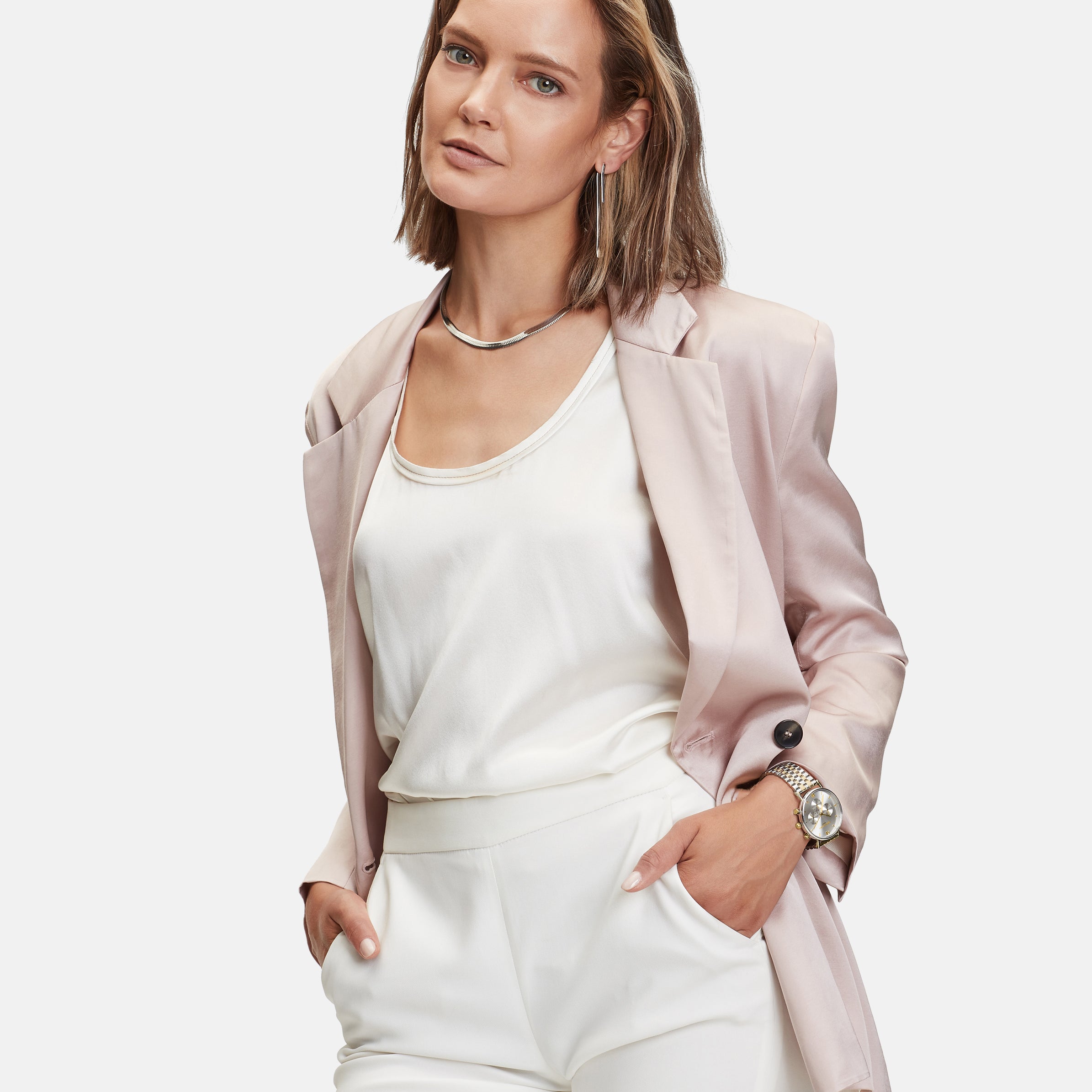 Eine Frau in einem hellrosa Blazer und weißem Outfit steht selbstbewusst mit den Händen in den Taschen, gestylt mit dem schicken LIEBESKIND BERLIN Set - Bicolor Edges von Liebeskind Berlin.
