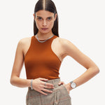 Eine Frau in einem orangefarbenen, ärmellosen Oberteil und einer karierten Hose posiert mit einer Hand an der Hüfte vor einem weißen Hintergrund. Dazu trägt sie die LIEBESKIND BERLIN Armbanduhr - The Chronograph von Liebeskind Berlin.