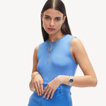 Frau in blauem ärmellosen Oberteil und Hose, mit Goldschmuck und der Liebeskind Berlin Armbanduhr - The Colorful Classic Must-Have, posiert vor einem weißen Hintergrund.