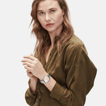 Frau in einem olivgrünen Kleid, die die LIEBESKIND BERLIN Armbanduhr - The Colorful Multifunction von Liebeskind Berlin trägt, posiert vor einem weißen Hintergrund und schaut in die Kamera.