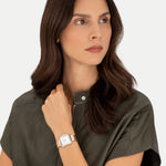 Frau mit langen braunen Haaren, trägt ein grünes Oberteil mit Reißverschluss und eine goldene Liebeskind Berlin Armbanduhr - The Classic Square, schaut nach links.