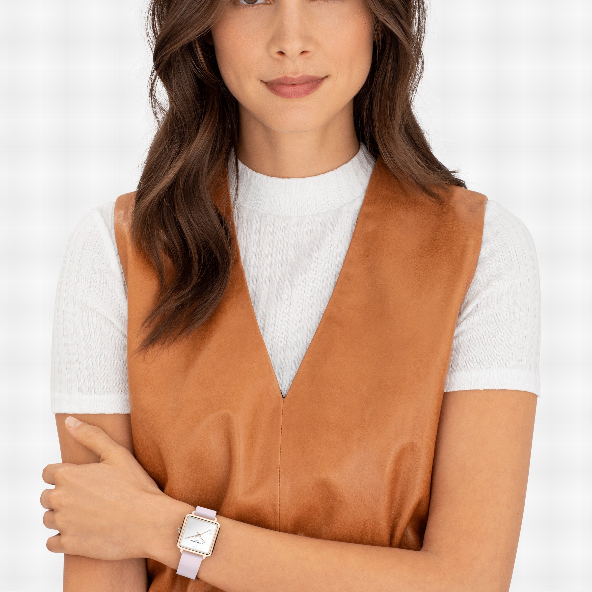 Frau mit gewellten braunen Haaren trägt eine braune Weste, ein weißes Oberteil und die LIEBESKIND BERLIN Armbanduhr - The Classic Square von Liebeskind Berlin, die sich durch skandinavisch inspiriertes Design auszeichnet.