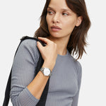 Frau in einem gerippten grauen langärmeligen Oberteil, die die stilvolle Liebeskind Berlin Armbanduhr - The Round Staple trägt, mit Blick nach links.