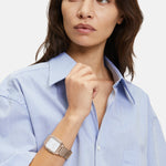 Eine Frau im hellblauen Button-up-Hemd trägt die Liebeskind Berlin Armbanduhr - The Modern Staple mit rechteckigem Gehäuse, während sie zur Seite schaut.