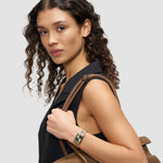Frau mit lockigem Haar trägt ein schwarzes ärmelloses Oberteil, hat eine braune Tasche dabei und zeigt die LIEBESKIND BERLIN Armbanduhr - Small Retro von Liebeskind Berlin, die ihren schicken Stil perfekt unterstreicht.