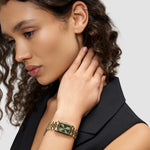 Frau mit lockigem Haar trägt ein schwarzes ärmelloses Oberteil und die Liebeskind Berlin Armbanduhr - Small Retro, die ihren Hals berührt.