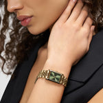 Eine Frau in Schwarz berührt ihren Hals und trägt die LIEBESKIND BERLIN Armbanduhr - Small Retro von Liebeskind Berlin mit goldenem Gehäuse und grünem Zifferblatt.