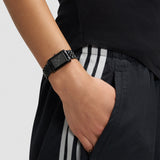 Stilvolles Accessoire: Die LIEBESKIND BERLIN Armbanduhr - Small Retro am Handgelenk, dazu schwarze Athletic-Pants mit weißen Streifen und die Hand lässig in der Tasche.