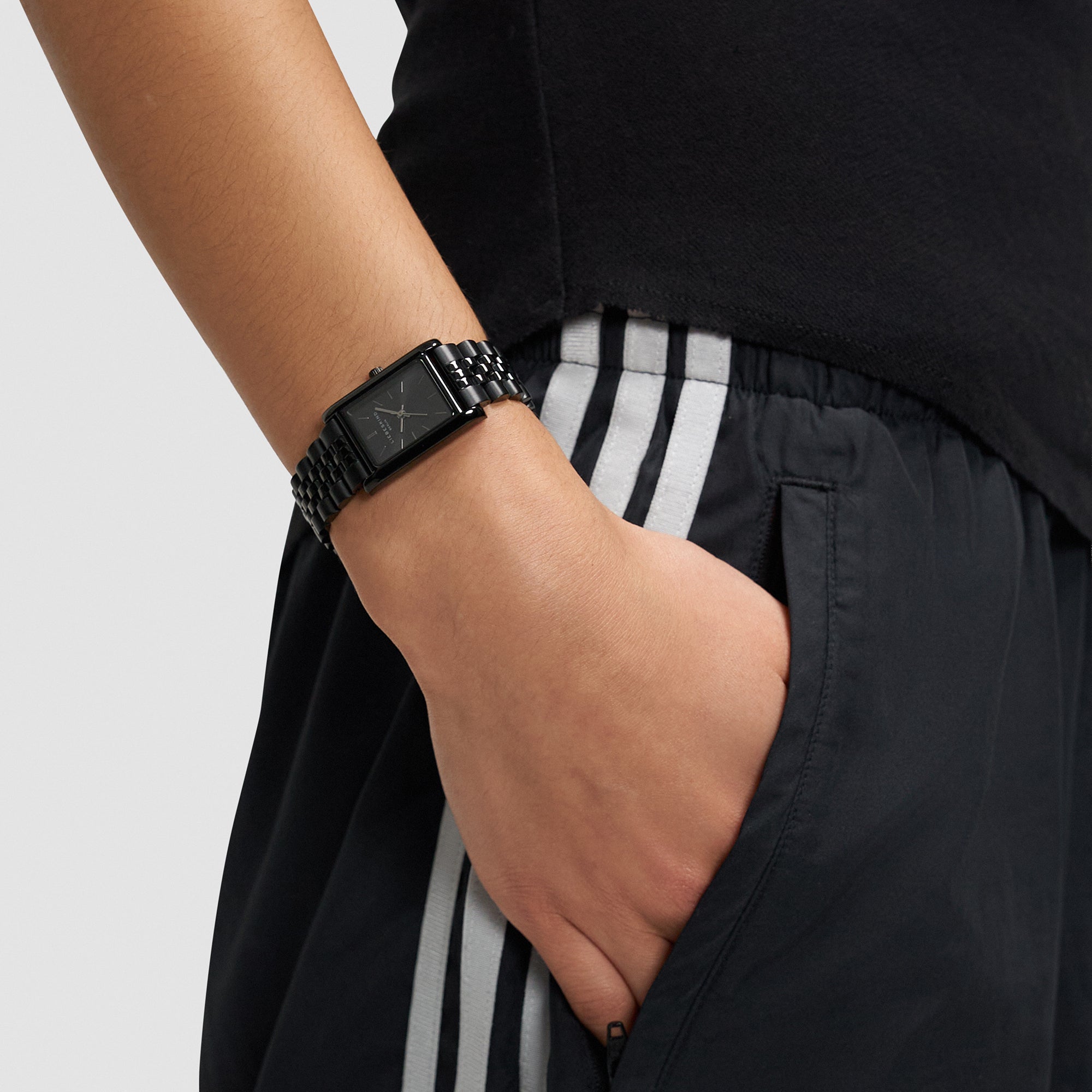 Stilvolles Accessoire: Die LIEBESKIND BERLIN Armbanduhr - Small Retro am Handgelenk, dazu schwarze Athletic-Pants mit weißen Streifen und die Hand lässig in der Tasche.