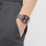 Person trägt eine graue Hose mit einer Liebeskind Berlin Armbanduhr - Vintage Classic mit rotem Zifferblatt und Retro-Stil. Das silberne Edelstahlmeshband verleiht dieser Vintage-inspirierten Uhr von Liebeskind Berlin einen modernen Touch.