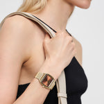 Frau im schwarzen Oberteil trägt eine goldene Liebeskind Berlin Armbanduhr - Vintage Classic mit Edelstahlmeshband und trägt einen beigen Taschenriemen über der Schulter.