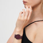 Frau trägt ein ärmelloses schwarzes Top und eine kastanienbraune LIEBESKIND BERLIN Armbanduhr - The Modern Must-Have by Liebeskind Berlin mit Meshband, die ihr Gesicht berührt.