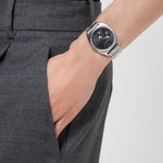 Eine Person in grauer Hose mit einer Hand in der Tasche, die eine silberne Liebeskind Berlin Armbanduhr - The Multifunction präsentiert.