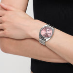 Eine Person mit verschränkten Armen, die ein schwarzes ärmelloses Oberteil und eine Liebeskind Berlin Armbanduhr - The Colorful Multifunction mit silbernem Edelstahlband und rosa Zifferblatt trägt.