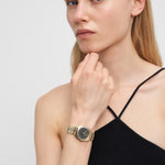 Eine Frau mit schwarzem Trägertop trägt die LIEBESKIND BERLIN Armbanduhr - The Classic Must-Have von Liebeskind Berlin und wirkt nachdenklich vor einem schlichten Hintergrund.