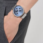 Eine Person trägt eine LIEBESKIND BERLIN Armbanduhr - Modern Chronograph von Liebeskind Berlin mit silbernem Gehäuse, blauem Zifferblatt und Edelstahlarmband, Hand in der Tasche.