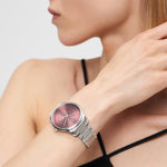 Eine Frau trägt eine silberne LIEBESKIND BERLIN Armbanduhr - Classic x Trends mit rosafarbenem Ziffernblatt und schwarzem Armband, die Hand am Hals - ein raffinierter Akzent des skandinavisch inspirierten Designs von Liebeskind Berlin.