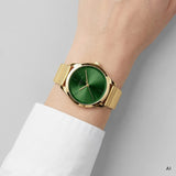 Ki generierte Detailaufnahme einer LIEBESKIND BERLIN Damen Armbanduhr mit grünem Zifferblatt, goldfarbenem Gehäuse und goldfarbenem Edelstahlarmband am Handgelenk getragen