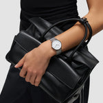 Eine Person in Schwarz hält eine schwarze Handtasche und trägt die Liebeskind Berlin Pure Elegance Armbanduhr an ihrem linken Handgelenk.