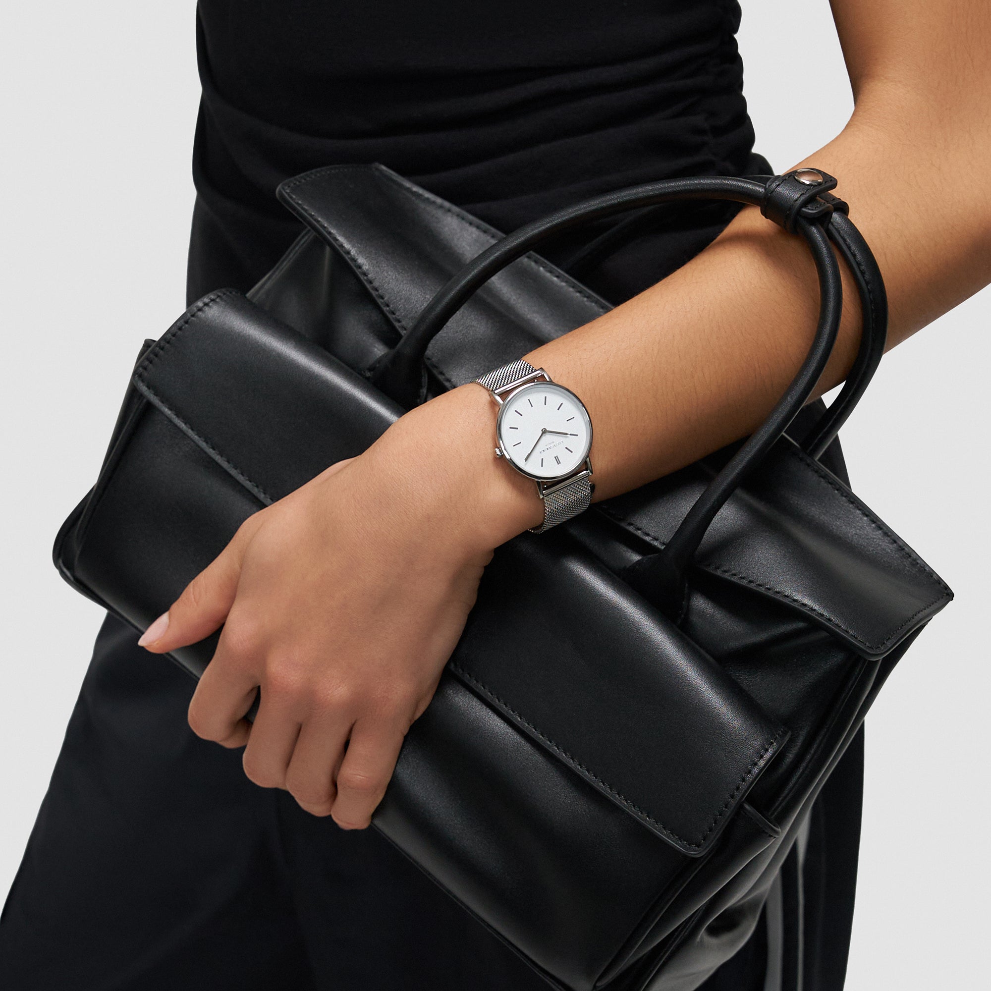 Eine Person in Schwarz hält eine schwarze Handtasche und trägt die Liebeskind Berlin Pure Elegance Armbanduhr an ihrem linken Handgelenk.