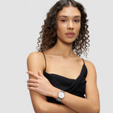 Eine Frau mit lockigem Haar in einem schwarzen Kleid trägt die Liebeskind Berlin Pure Elegance Armbanduhr und posiert vor einem schlichten hellgrauen Hintergrund.