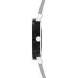 Seitenansicht der LIEBESKIND BERLIN Armbanduhr - Acetat Chic von Liebeskind Berlin im minimalistischen Design mit dunklem Zifferblatt, silberner Krone und hellgrauem Echtlederarmband auf weißem Hintergrund.