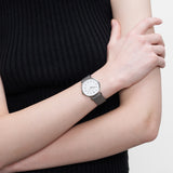 LIEBESKIND BERLIN Damenarmbanduhr mit weißem Zifferblatt und grauem Lederarmband am Handgelenk getragen.