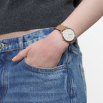 LIEBESKIND BERLIN Damenarmbanduhr in Gold mit weißem Zifferblatt und braunem Lederarmband am Handgelenk getragen.