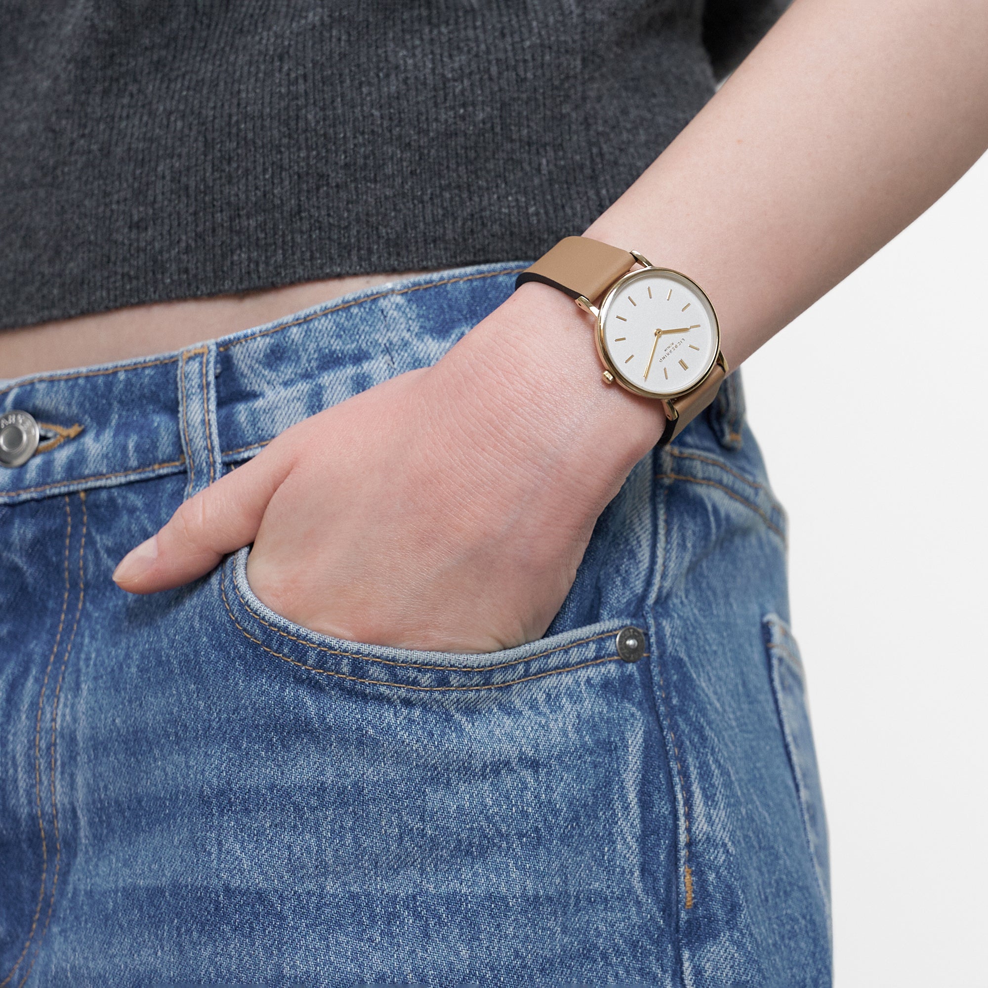 LIEBESKIND BERLIN Damenarmbanduhr in Gold mit weißem Zifferblatt und braunem Lederarmband am Handgelenk getragen.