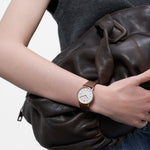 LIEBESKIND BERLIN Damenarmbanduhr in Roségold mit weißem Zifferblatt und braunem Lederarmband am Handgelenk getragen.