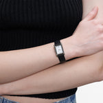 Rechteckige LIEBESKIND BERLIN Damenarmbanduhr mit schwarzem Lederarmband und weißem Zifferblatt am Handgelenk getragen.