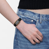 LIEBESKIND BERLIN Damenarmbanduhr mit goldfarbenem rechteckigem Gehäuse und schwarzem Lederarmband am Handgelenk getragen.