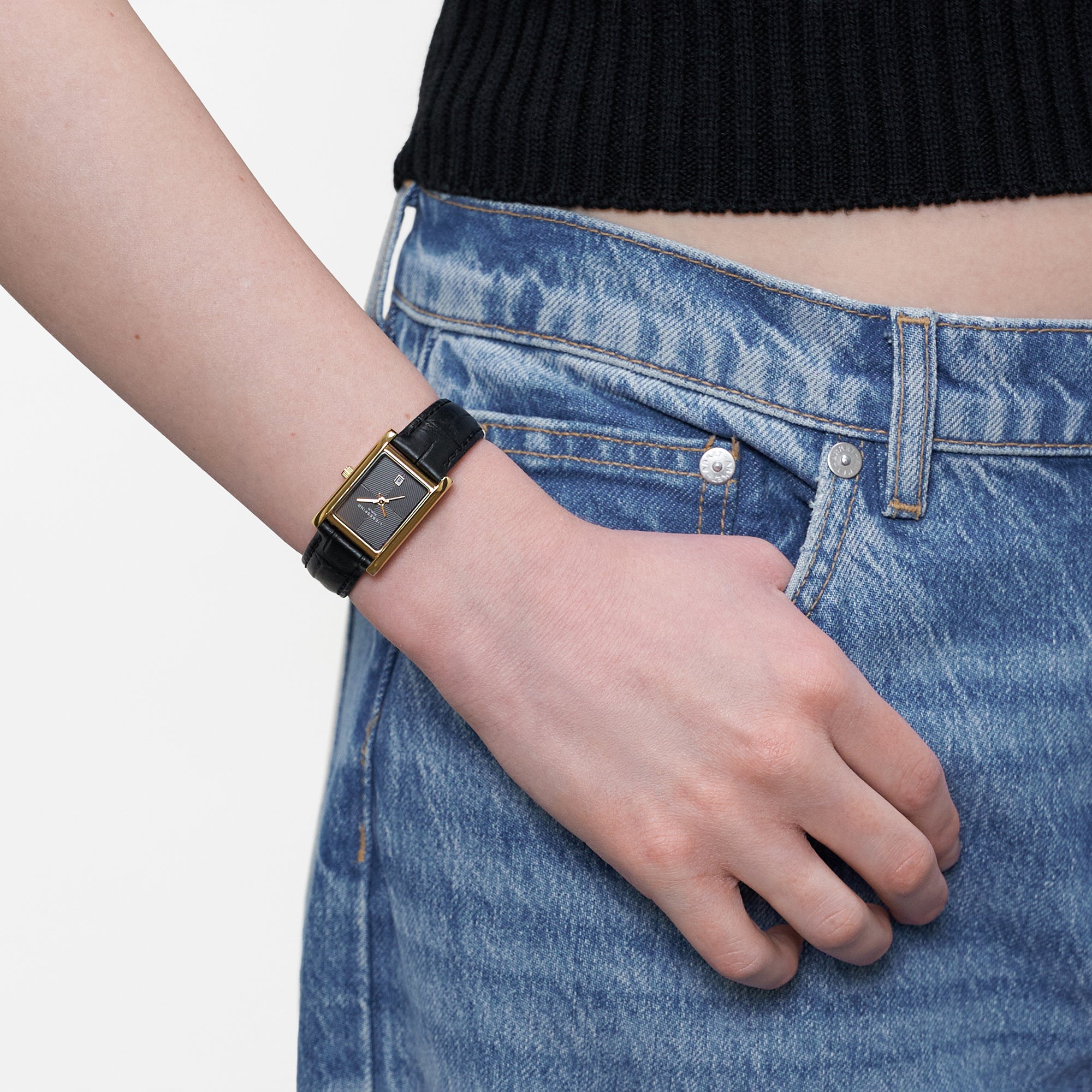 LIEBESKIND BERLIN Damenarmbanduhr mit goldfarbenem rechteckigem Gehäuse und schwarzem Lederarmband am Handgelenk getragen.