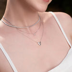 Frau trägt eine Ania Haie Halskette - Flache Schlangenkette aus 925 Sterling Silber, gestylt im Dreilagen-Look mit Kreuz- und Herzanhängern über einem weißen Top.