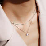 Nahaufnahme einer Person, die zwei zarte silberne Halsketten trägt, darunter die ANIA HAIE Halskette - Mother of Pearl von Ania Haie, kombiniert mit einem hellrosa Blazer.