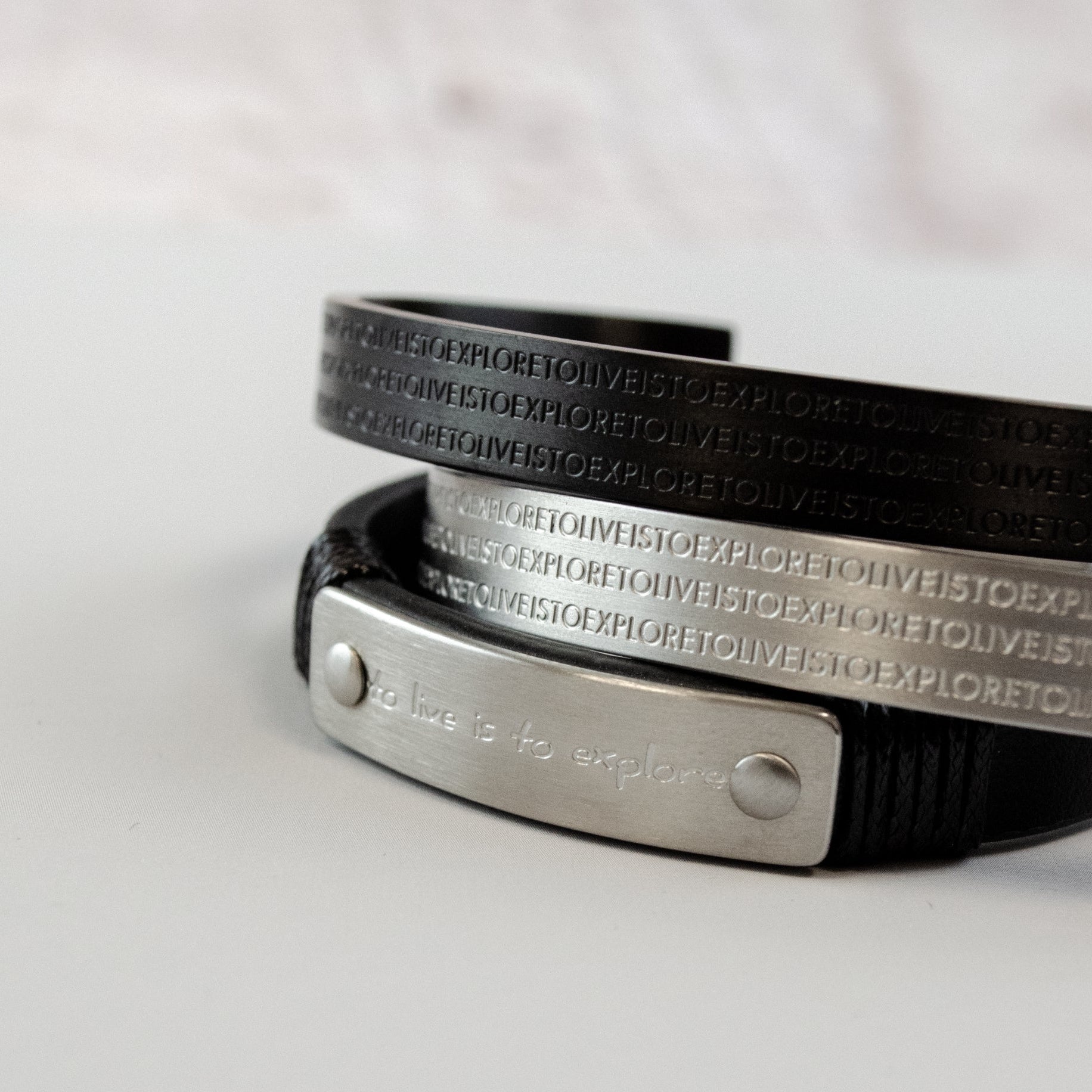 Herrenarmband aus schwarzem Leder mit Edelstahl-Elementen in Silber und Schwarz. Das mehrreihige Design kombiniert eine gravierte Metallplatte mit geprägten Edelstahlbändern und sorgt für einen markanten, modernen Look.
