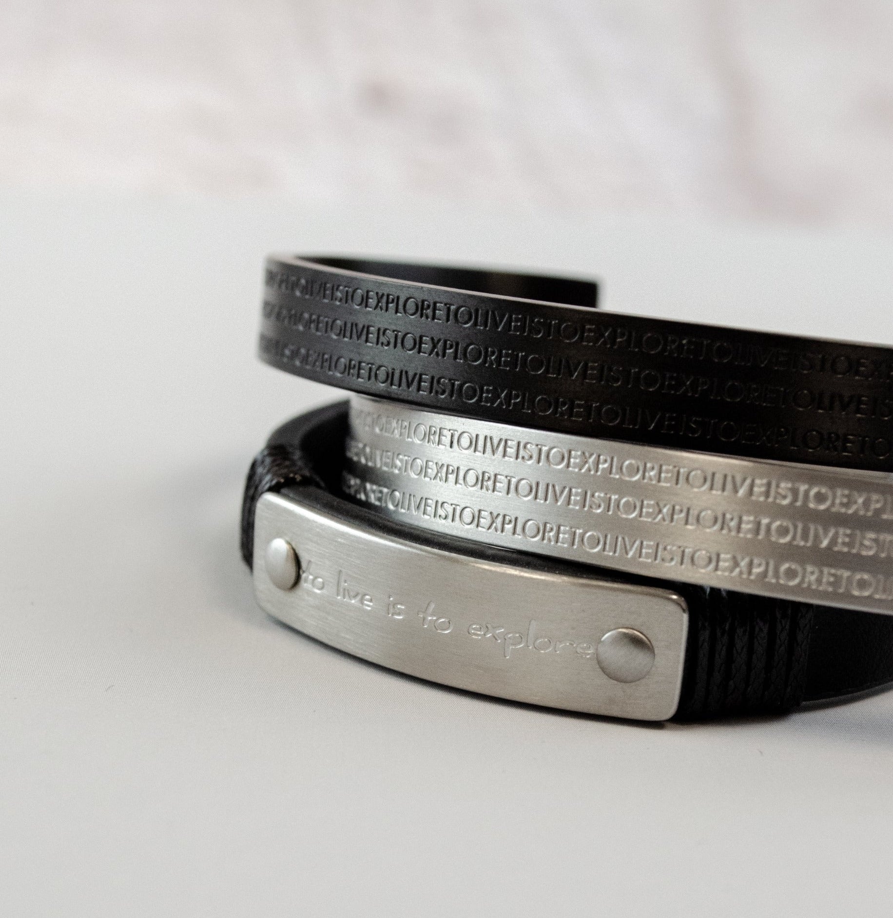 Herrenarmband aus schwarzem Leder mit Edelstahl-Elementen in Silber und Schwarz. Das mehrreihige Design kombiniert eine gravierte Metallplatte mit geprägten Edelstahlbändern und sorgt für einen markanten, modernen Look.