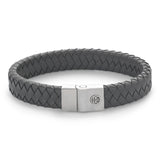 Das Rebel & Rose Armband - Full Metal Premium 12mm Grey besteht aus geflochtenem Leder und einem Edelstahlverschluss mit einer silbernen Schließe, in die ein kreisförmiges Logo eingraviert ist, das auf einem weißen Hintergrund abgebildet ist.
