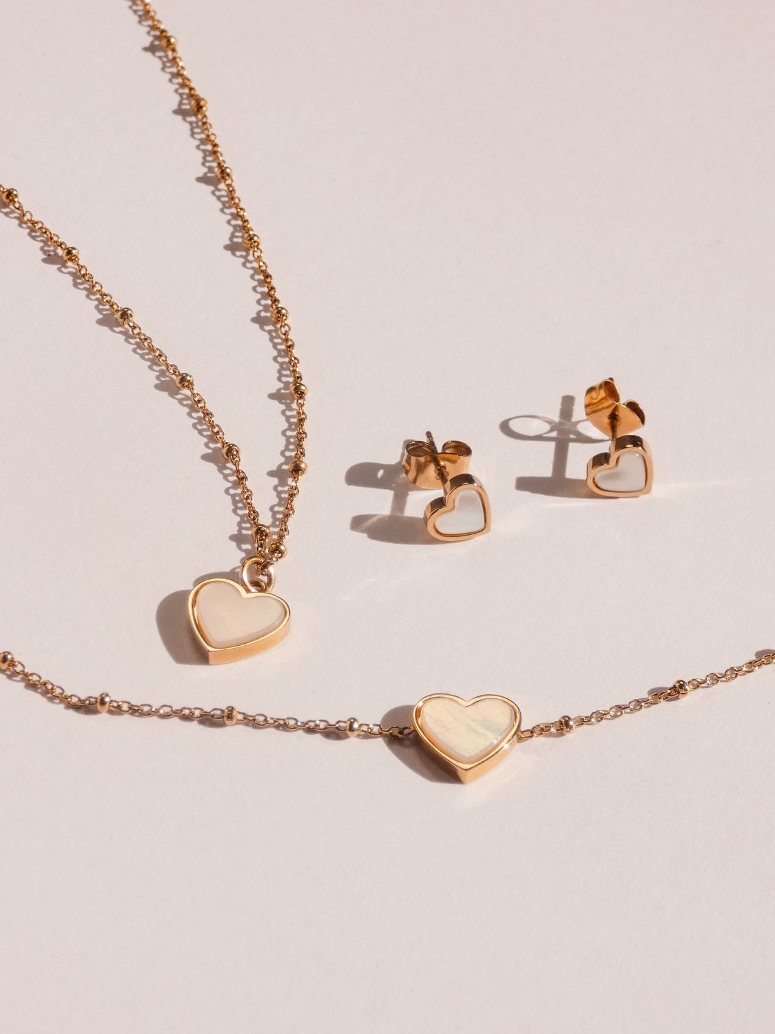 Neuheiten von s.Oliver: zarter goldfarbener Schmuck mit Herzmotiven, bestehend aus Kette, Armband und passenden Ohrsteckern, minimalistisch arrangiert auf hellem Hintergrund.